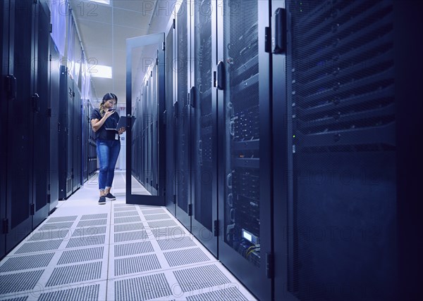 Female technician using laptop and phone in server room