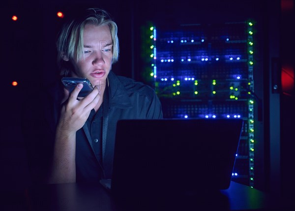 Technician using laptop and smart phone in server room