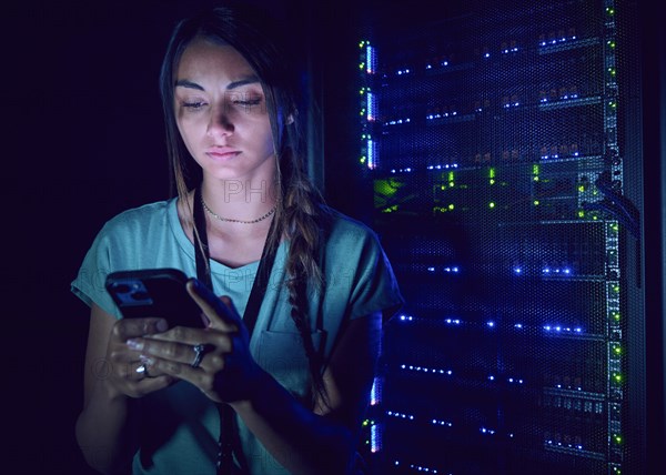 Female technician using smart phone in server room