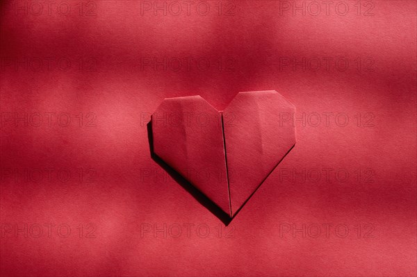 Red origami heart on red background