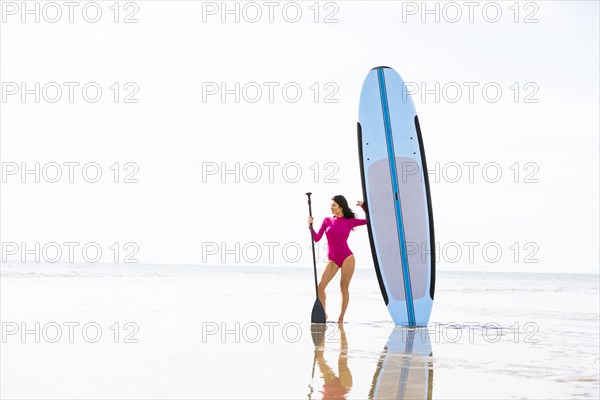 Woman standing next to paddleboard on sandy beach