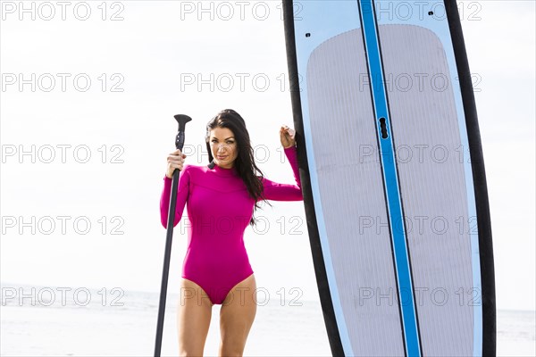 Woman standing next to paddleboard and holding oar