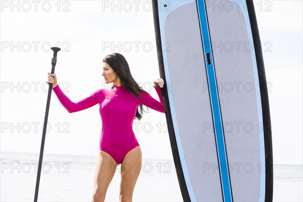 Woman holding oar next to paddleboard on beach