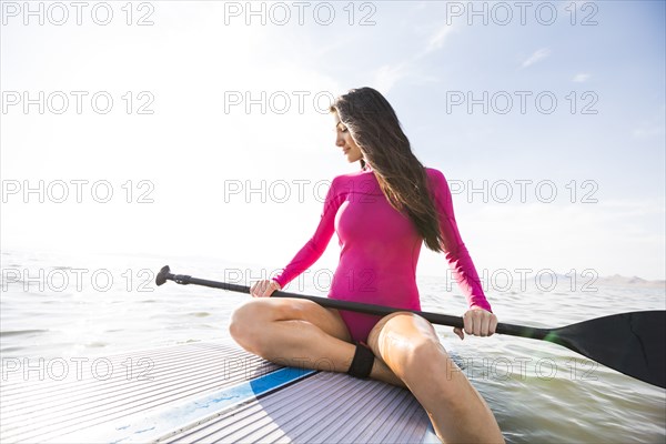 Woman holding oar and sitting on paddleboard