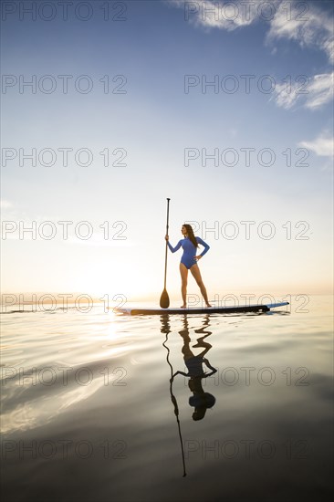 Woman standing on paddleboard at sunset