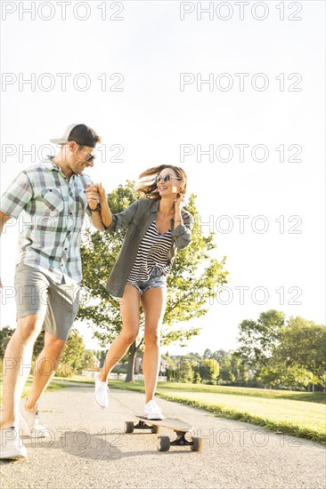 Man helping woman to balance while riding longboard