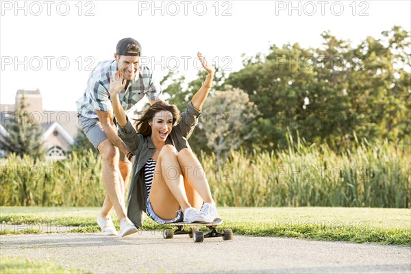 Man pushing woman sitting on longboard in park