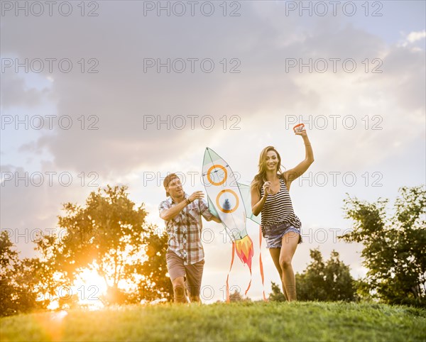 Woman and man running with kite in park at sunset