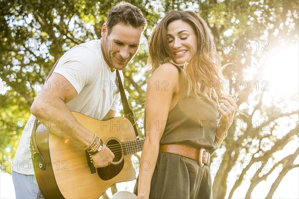 Woman dancing to music while man playing guitar in park