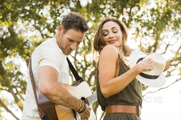 Man playing guitar and woman dancing in park