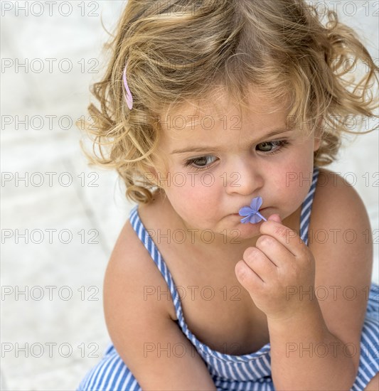 Cute blond girl smelling blue flower