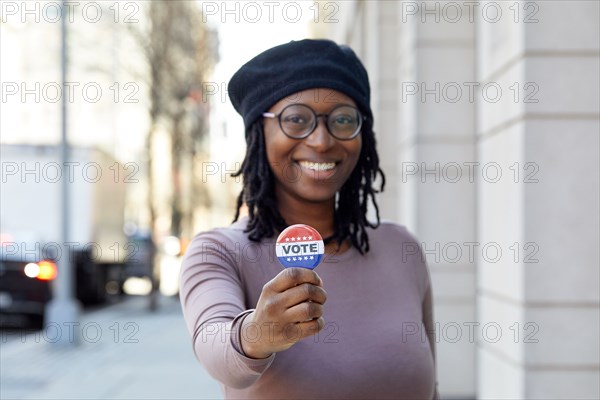 Portrait of smiling woman showing Vote button in city