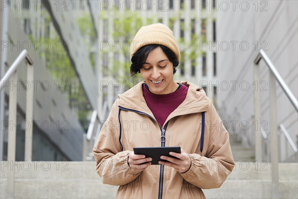 Smiling woman holding digital tablet on steps in city