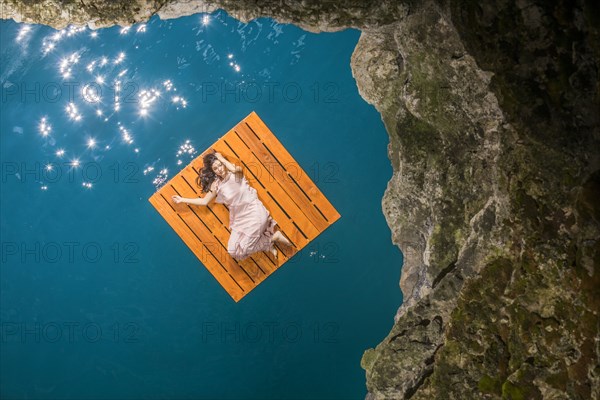 Overhead view of woman lying on floating dock near rocky coast