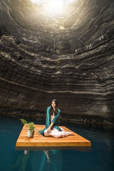 Portrait of woman sitting on floating dock near rocky coast