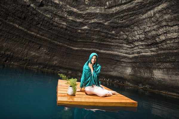 Portrait of woman sitting on floating dock near rocky coast