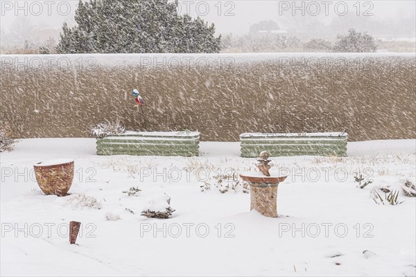 Garden with adobe wall and flowerpots in heavy snowfall