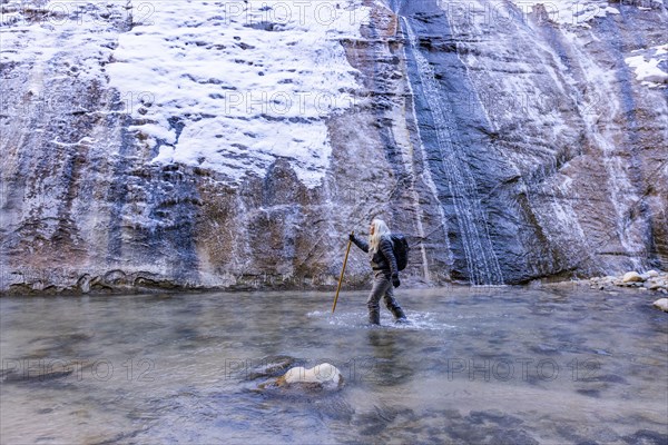 Senior woman crossing river while hiking in mountains