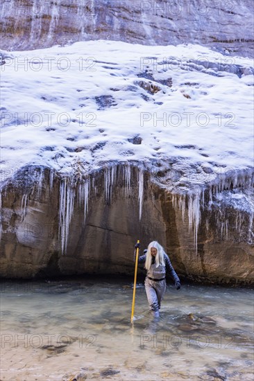 Senior woman crossing river while hiking in mountains