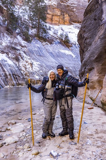 Senior couple crossing river while hiking in mountains