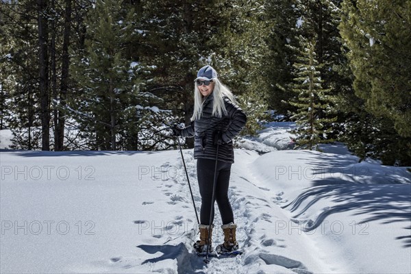 Senior woman wearing snowshoes hiking in snowy forest