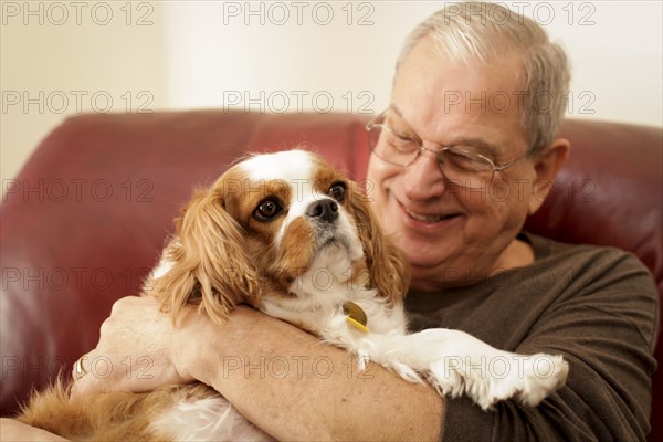 Senior man holding cavalier king charles spaniel at home