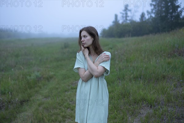 Woman standing in meadow on foggy day