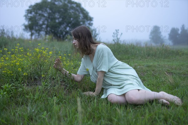 Woman looking at flowers in meadow on foggy day