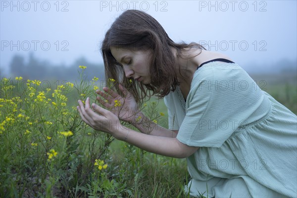 Woman smelling flowers in meadow on foggy day