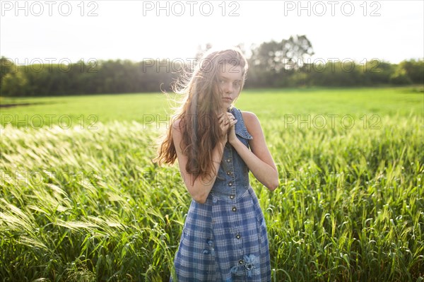 Portrait of woman standing with hands clasped in field