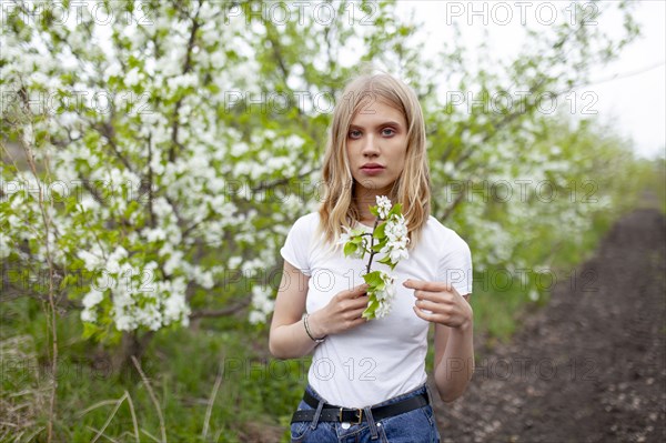 Portrait of woman holding branch of apple tree in orchard