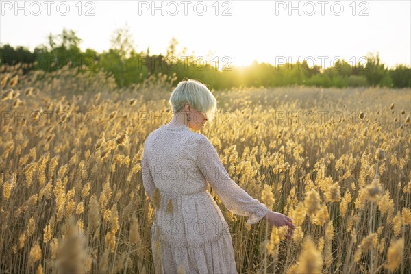 Young woman standing in field and touching plants at sunset