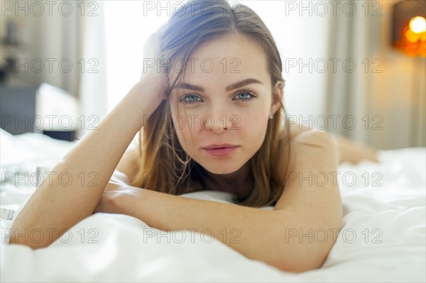 Portrait of woman lying on bed and looking at camera at home