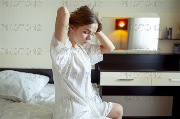 Young woman sitting on bed in pajamas