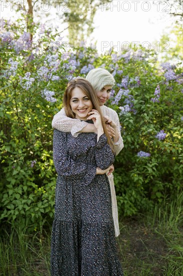 Portrait of young women embracing against lilac bush in garden