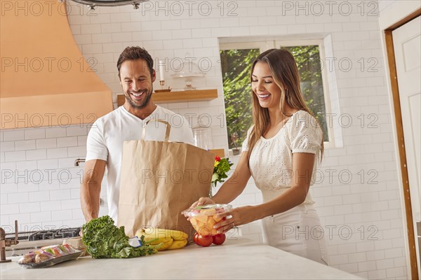 Smiling couple with paper shopping bag and groceries in kitchen