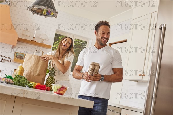 Smiling couple with paper shopping bag and groceries in kitchen