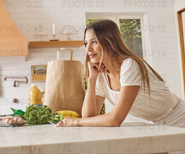 Smiling woman with paper shopping bag and groceries in kitchen