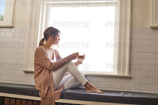 Woman relaxing with cup of tea by window at home