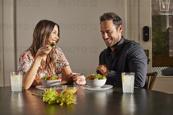 Smiling couple enjoying salad at table at home