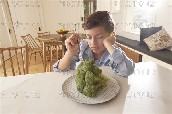 Displeased boy looking at broccoli on plate