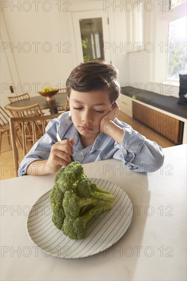 Displeased boy looking at broccoli on plate