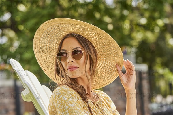 Woman in straw hat and sunglasses relaxing in park