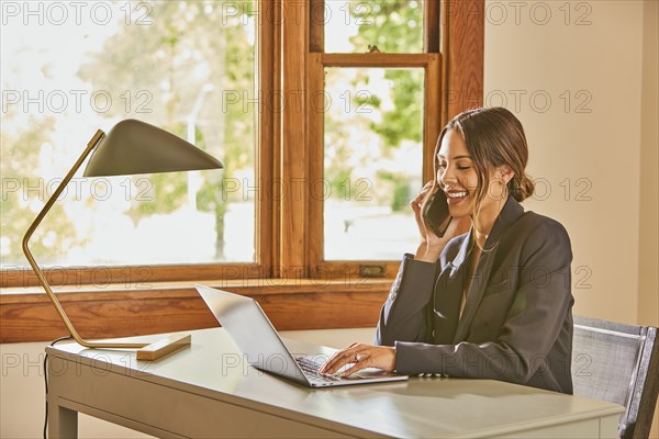 Smiling woman using laptop and smart phone at desk at home