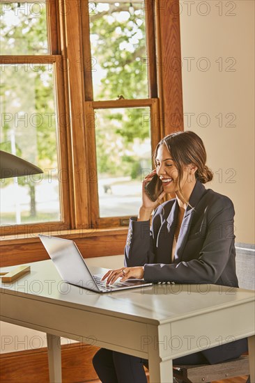 Smiling woman using laptop and smart phone at desk at home