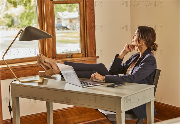 Woman relaxing at desk with laptop at home