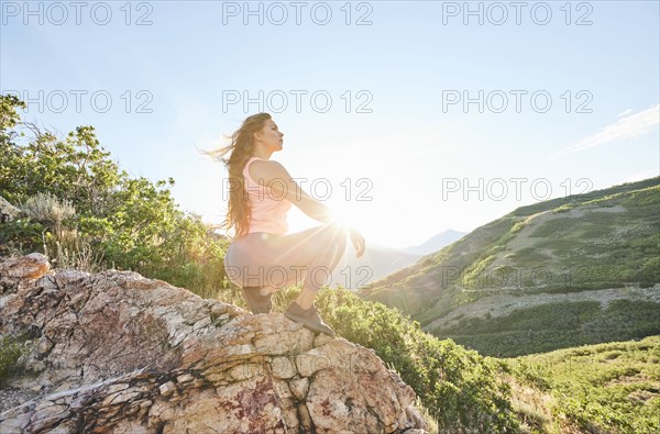 Mid adult woman crouching on rock during hike