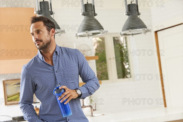 Mid adult man standing in kitchen with water bottle