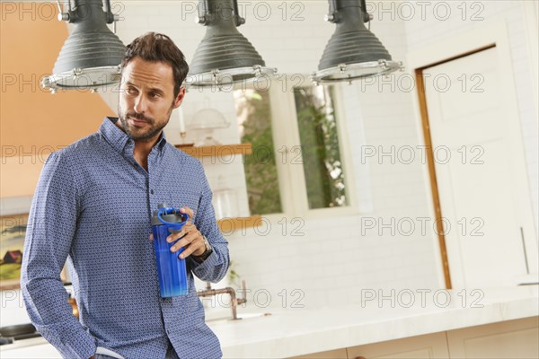 Mid adult man standing in kitchen with water bottle