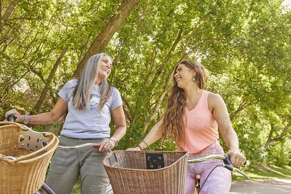 Mother and adult daughter riding bicycles in park